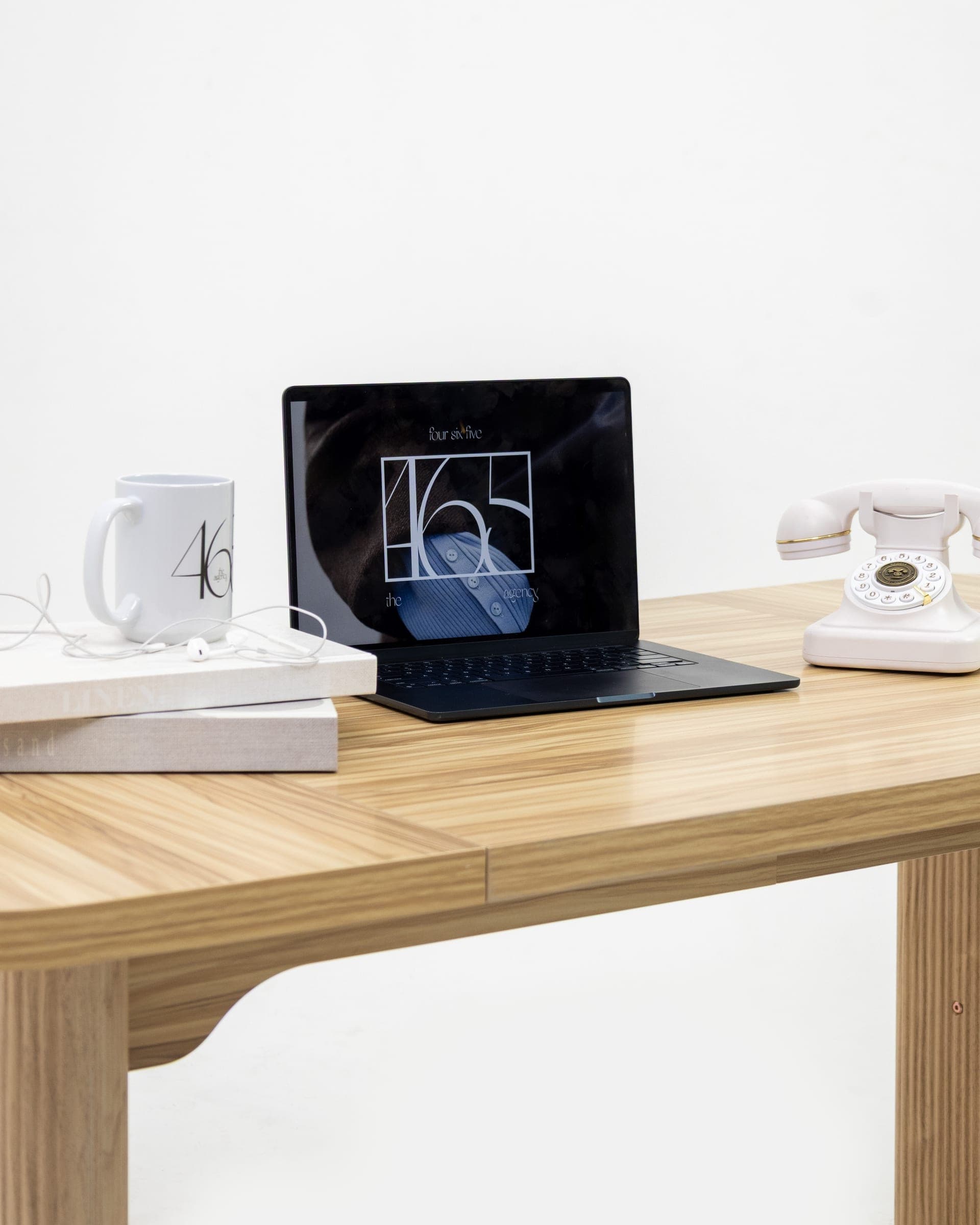 The 465 studio desk: the new identity on screen beside the brand's mug and a white rotary phone