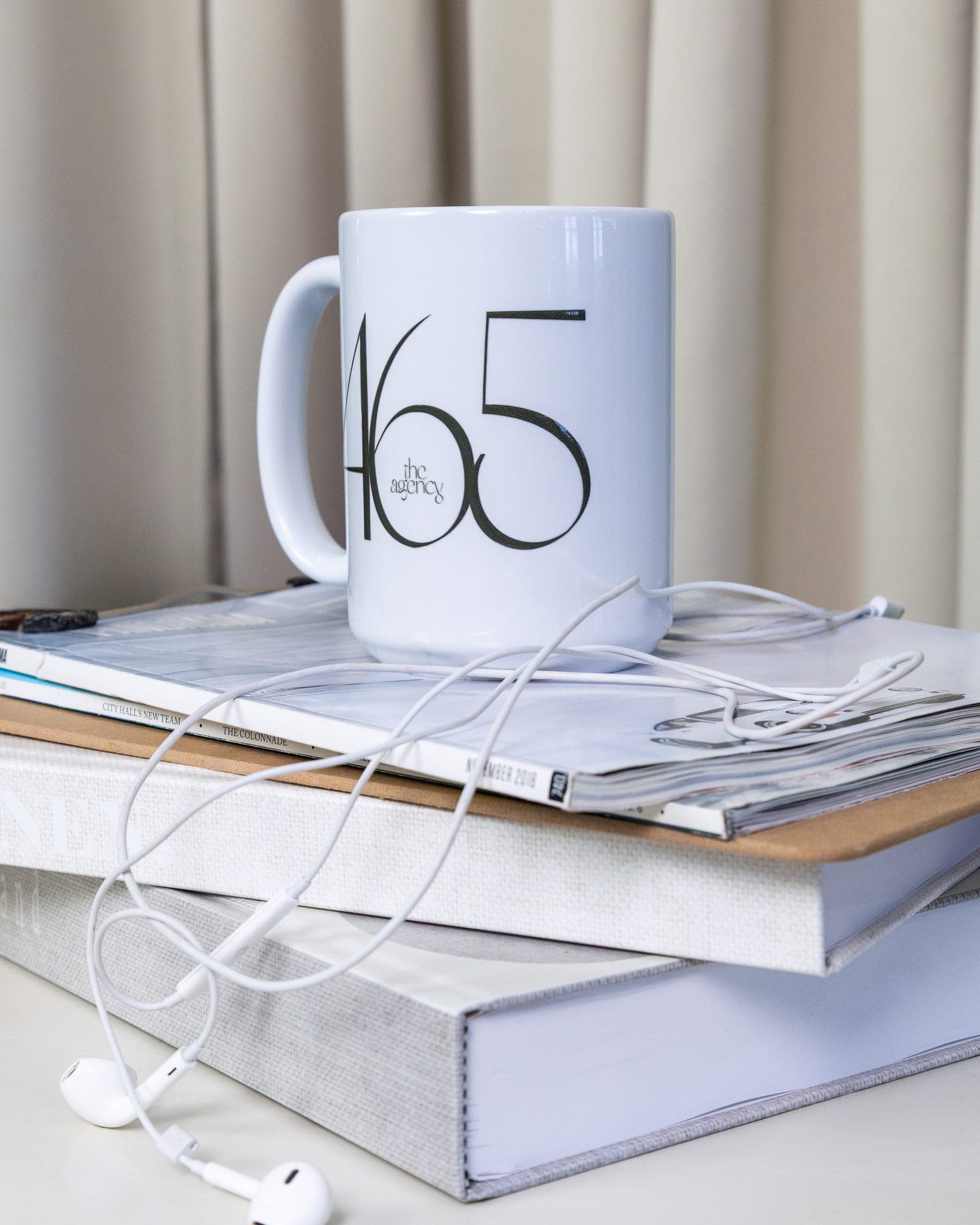 A 465 mug resting on a stack of design books with earbuds